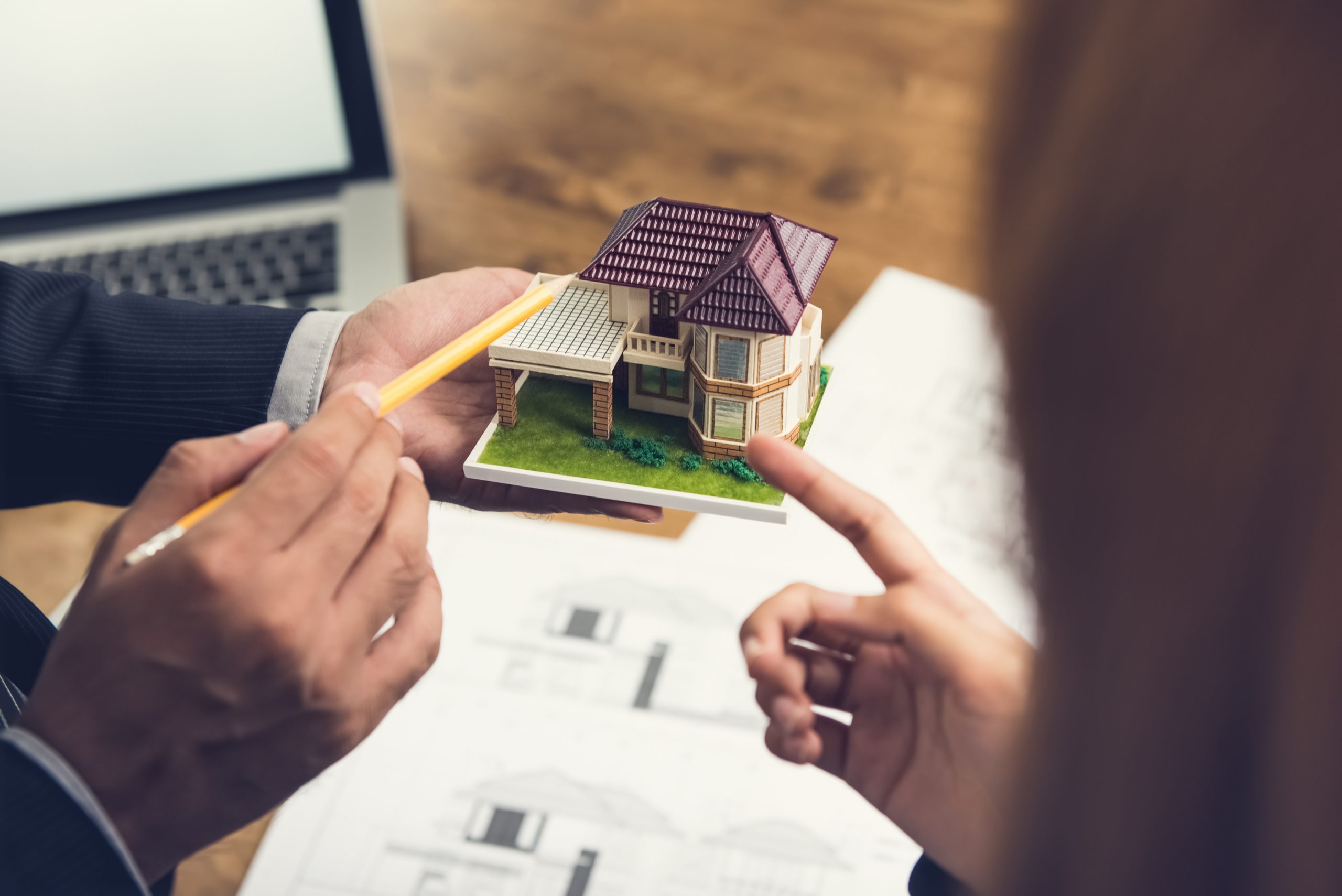 Housing developer agent holding an architectural model and explaining concept to client or architect for real estate development.